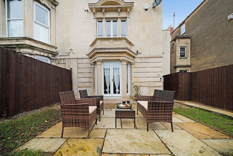 Rear garden patio with two wicker chairs, stone paving, and cream-coloured townhouse