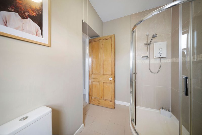 Modern bathroom with walk-in shower, toilet, wooden door and neutral tile flooring