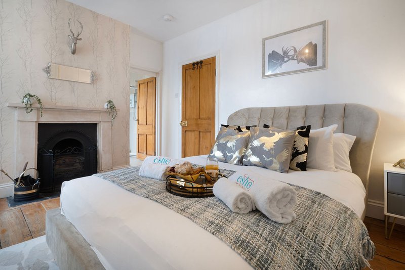 Bedroom with fireplace, upholstered bed, rolled towels, cushions and framed wall art