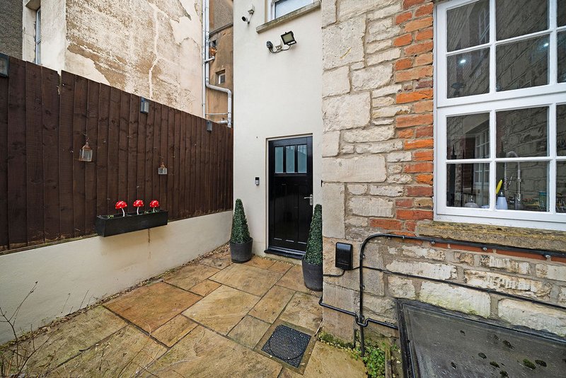 Rear courtyard with paved ground, brick walls, dark wooden gate and potted plants