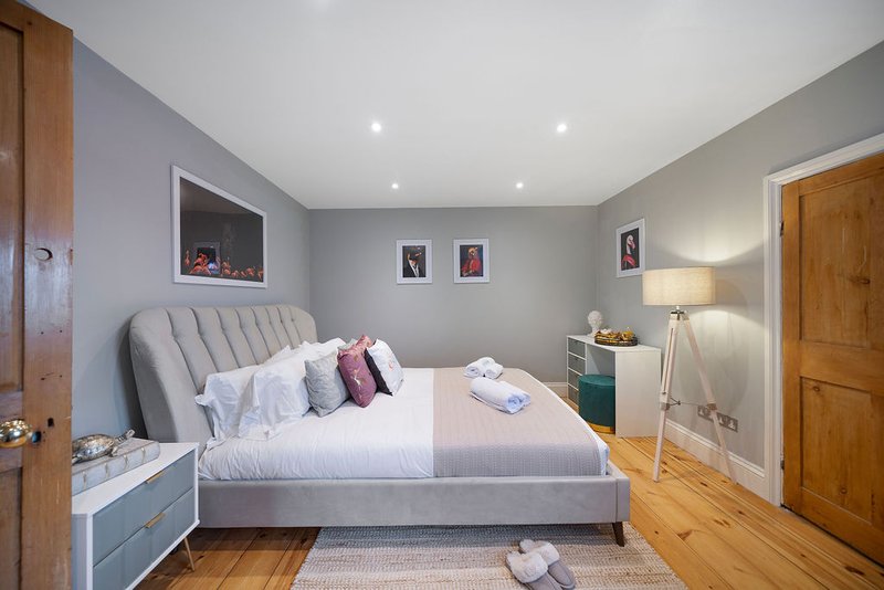 Modern bedroom with gray upholstered bed, wooden flooring, bedside lamps, and framed artwork on walls
