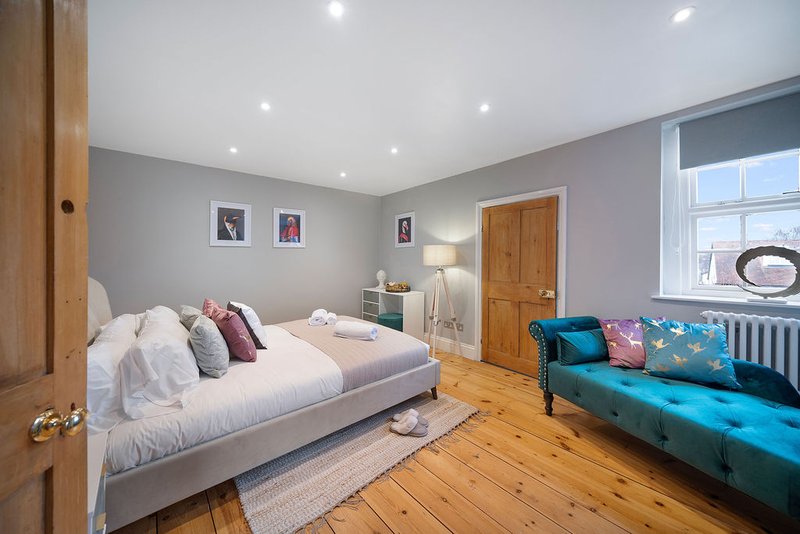 Spacious bedroom with double bed, wooden flooring, grey walls, and teal sofa seating area