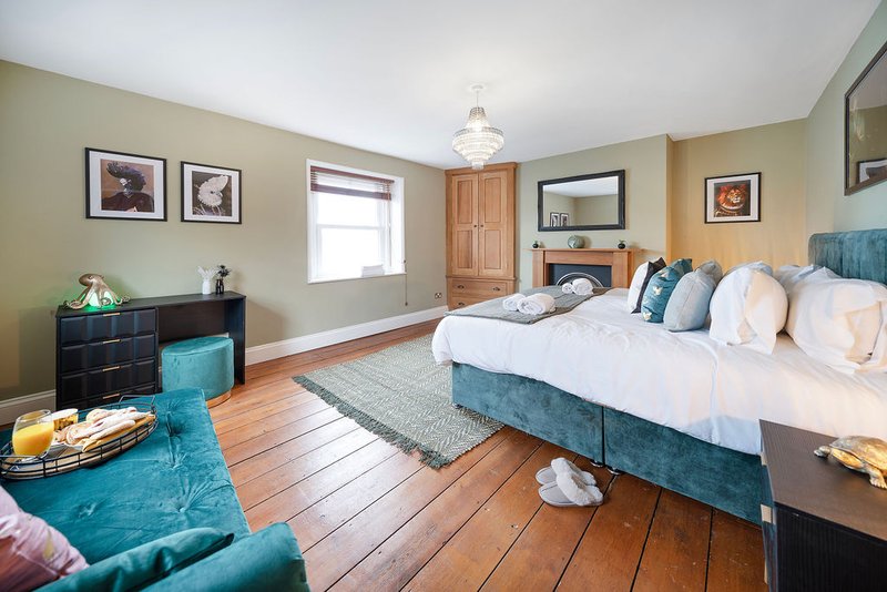 Spacious bedroom with double bed, turquoise upholstered furniture, wooden floor and framed wall art