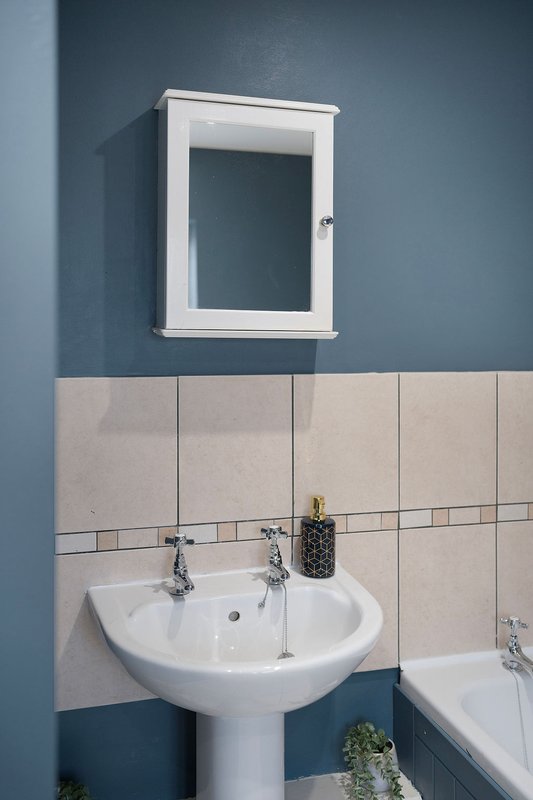 Bathroom with pedestal sink, wall-mounted cabinet, tiled walls and bathtub
