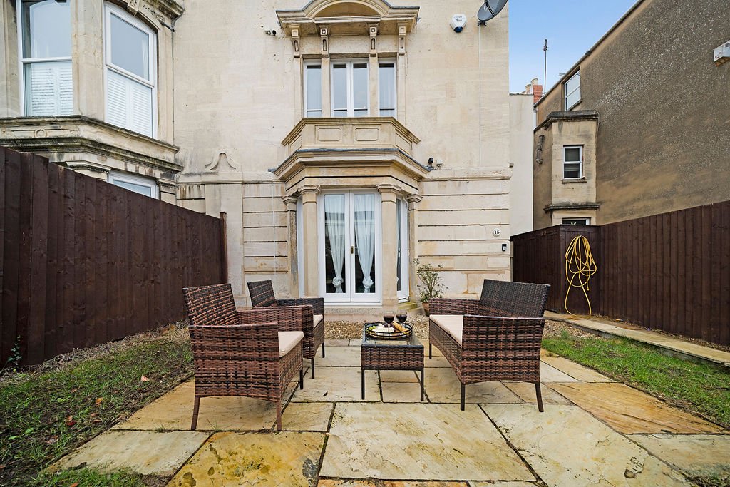 Rear garden patio with two rattan chairs, stone paving and townhouse backdrop