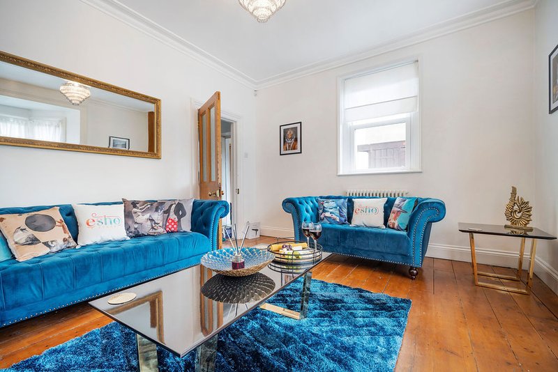 Bright living room with blue velvet sofas, wooden floor, large mirror and windows