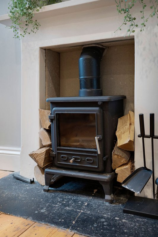Black wood-burning stove with chimney pipe in alcove, firewood stacked beside it