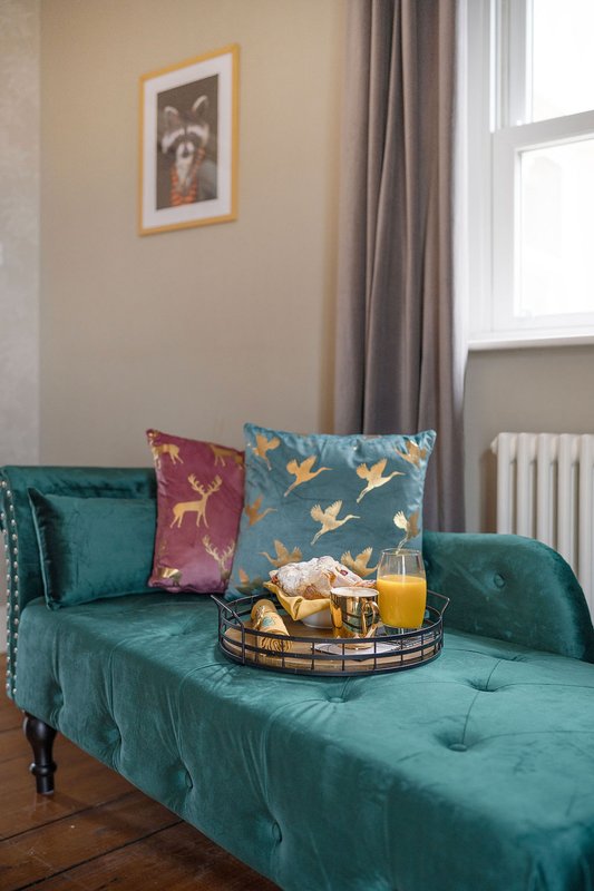 Teal velvet sofa with decorative pillows, window with curtains, framed wall art