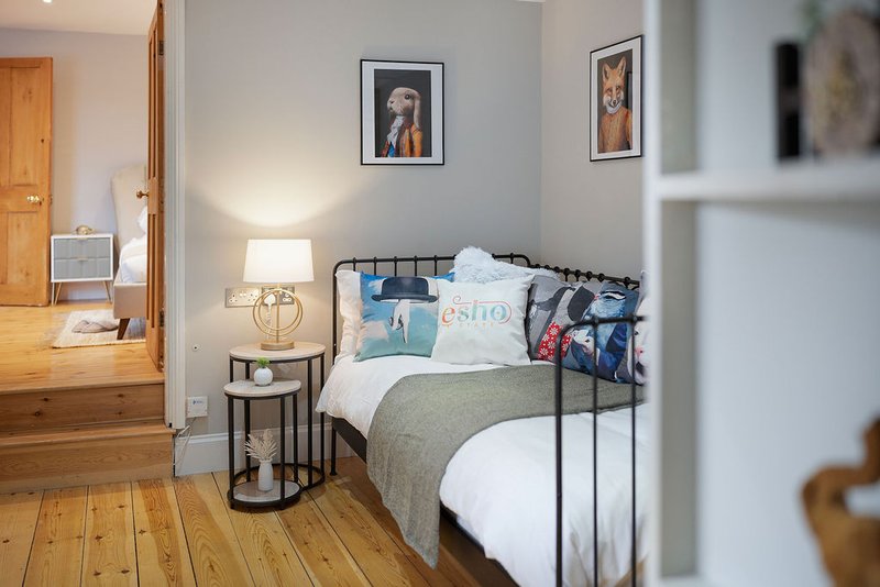 Bright bedroom with metal-frame bed, bedside lamp, wooden flooring and framed wall art