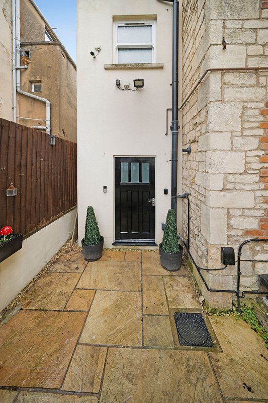 Narrow courtyard entry with black door, stone paving, potted plants and brick walls