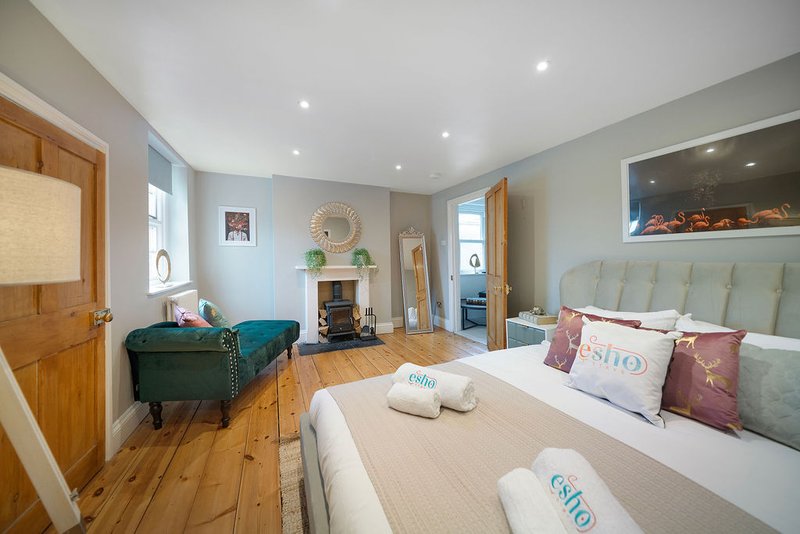 Spacious bedroom with double bed, wooden floor, teal armchair, and fireplace