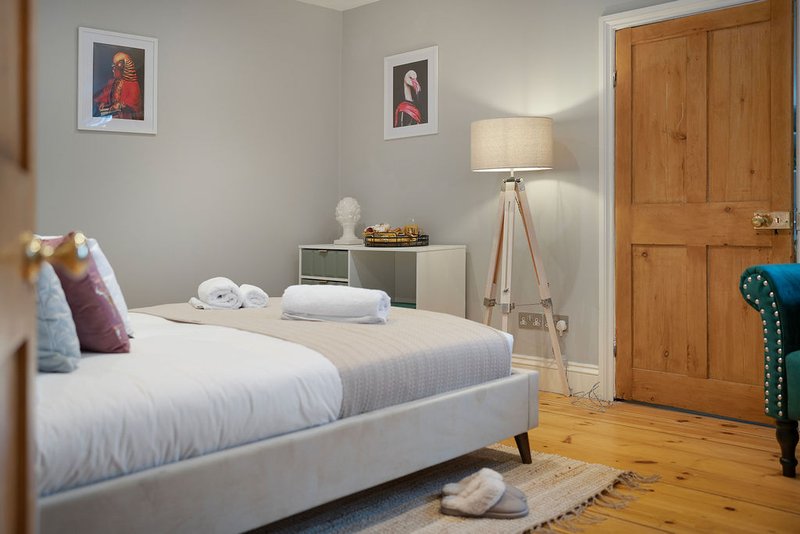 Modern bedroom with white bed, wooden wardrobe, tripod lamp and framed wall art