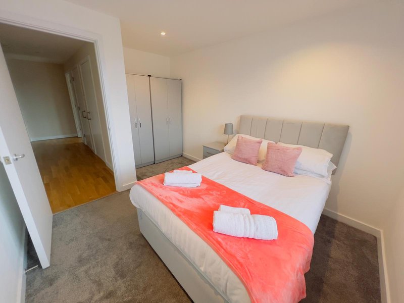 Modern bedroom with double bed, pink pillows, red throw, white towels and wardrobe