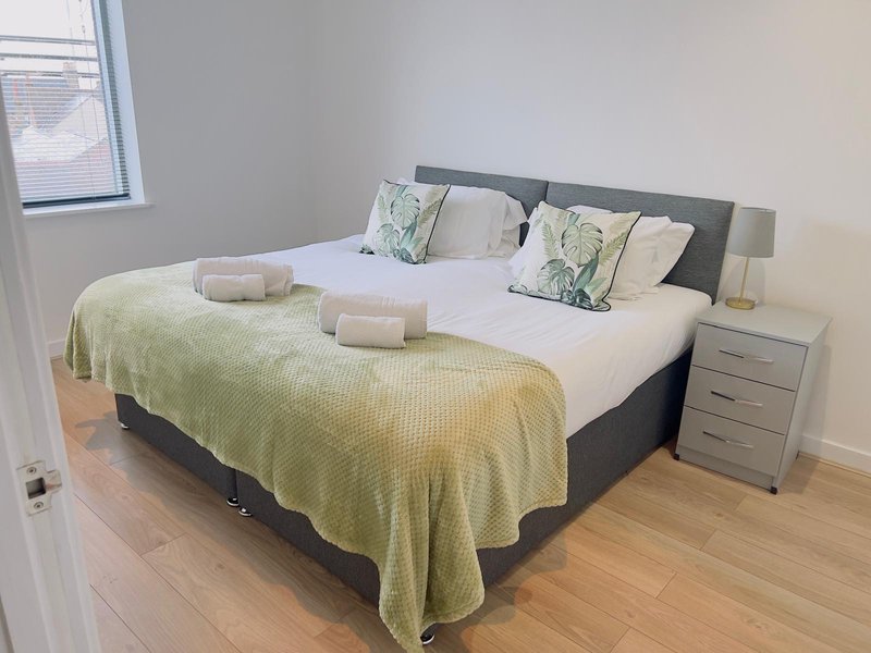 Bedroom with double bed, green throw, decorative pillows, wooden floor and bedside table