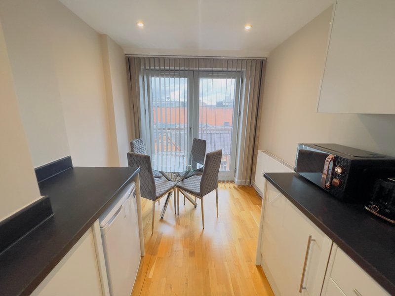 Modern open-plan kitchen and dining area with black counters, wooden floor, and glass balcony doors
