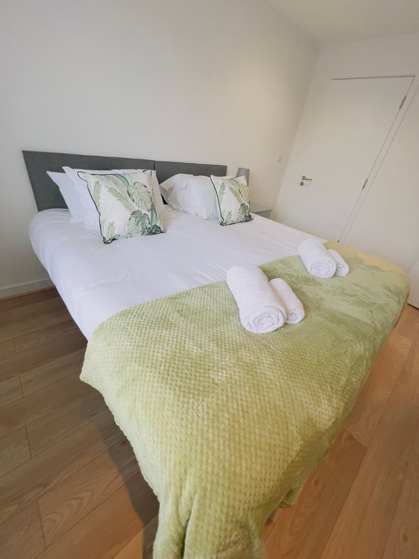 Bedroom with double bed, white pillows, green bedding, wooden floor and grey headboard