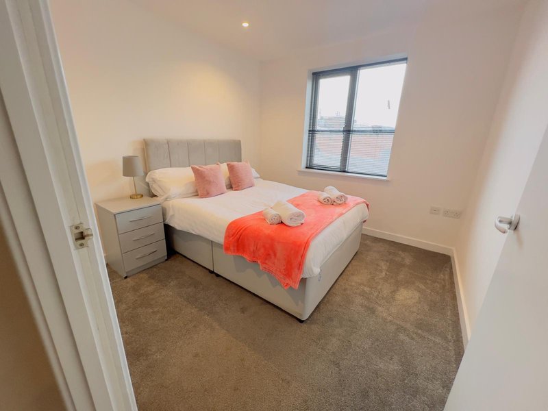 Modern bedroom with double bed, beige headboard, pink cushions, orange throw, and bedside table
