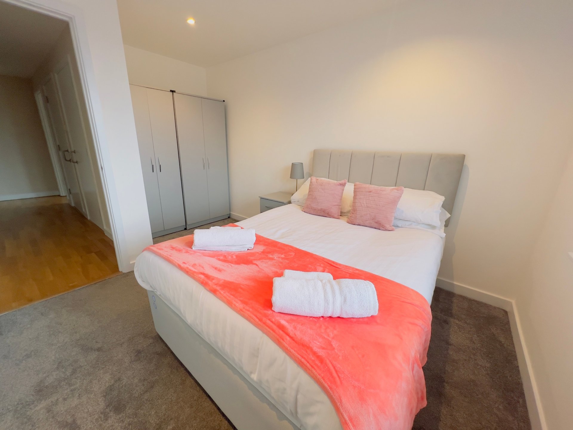 Bedroom with double bed, pink pillows, red throw, white towels, wardrobe and door