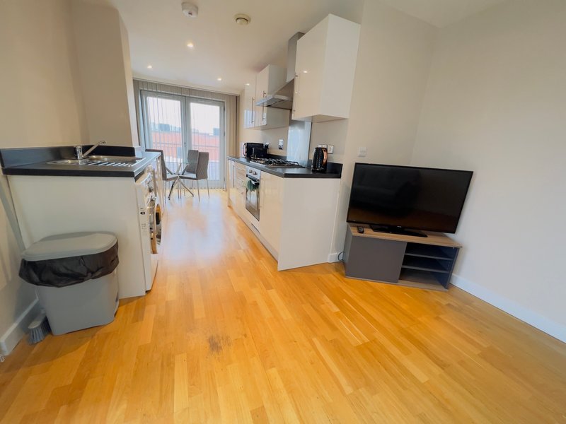 Open-plan kitchen and living area with wooden flooring, white cabinetry, and television
