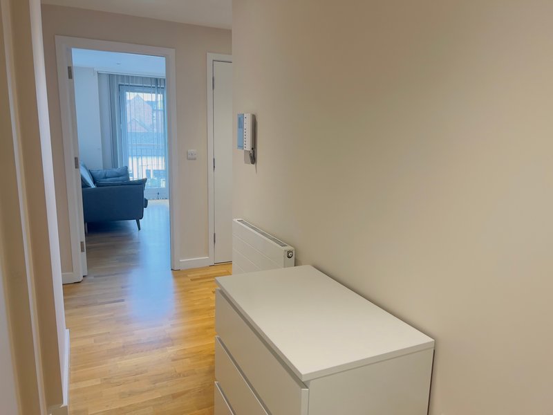 Hallway with wooden flooring, white dresser, and open doorway to living area