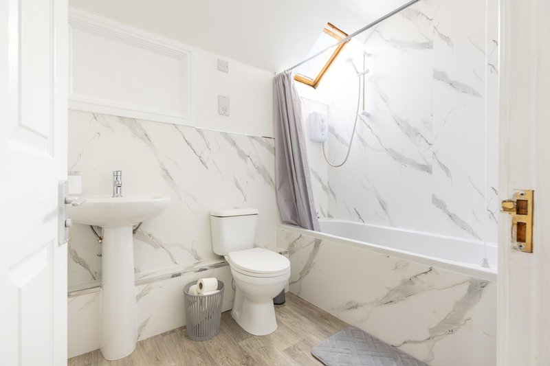 Modern bathroom with marble tiles, white pedestal sink, toilet, and shower enclosure with gold fixtures