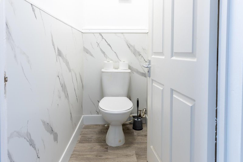 Small bathroom with white toilet, marble-effect wall tiles and wooden floor