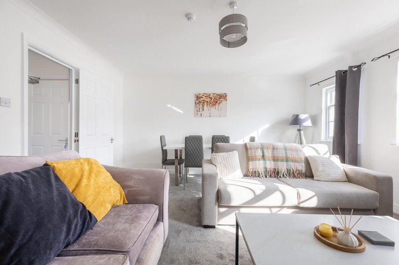 Open-plan living room with grey sofas, yellow cushions, dining chairs and pendant light