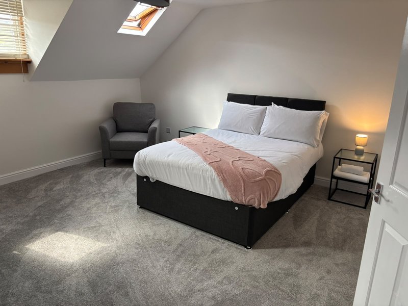 Bright attic bedroom with double bed, grey armchair, bedside table and skylight window