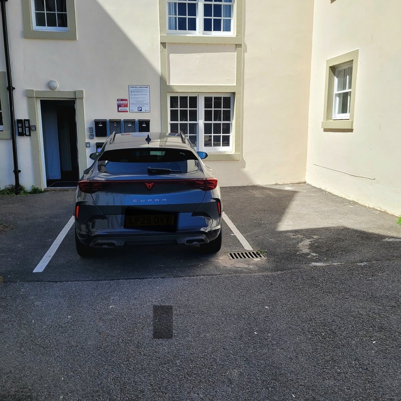 Exterior parking area with black car parked in marked space, cream-colored building with windows visible
