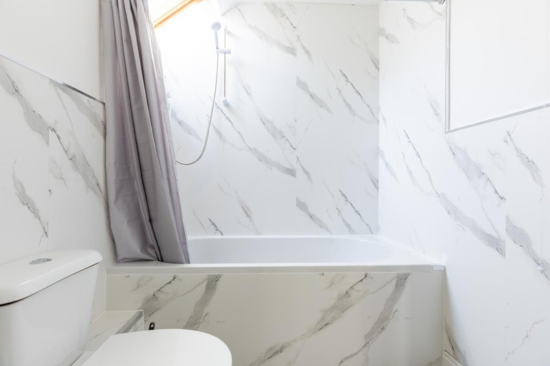 Modern bathroom with marble-effect tiles, white toilet, bathtub and shower enclosure