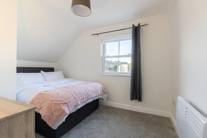 Bright attic bedroom with double bed, window with black curtains, wooden bedside table and ceiling lamp