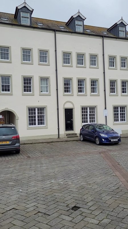 Cream-coloured townhouse with dormer windows, parked cars in front on brick paving