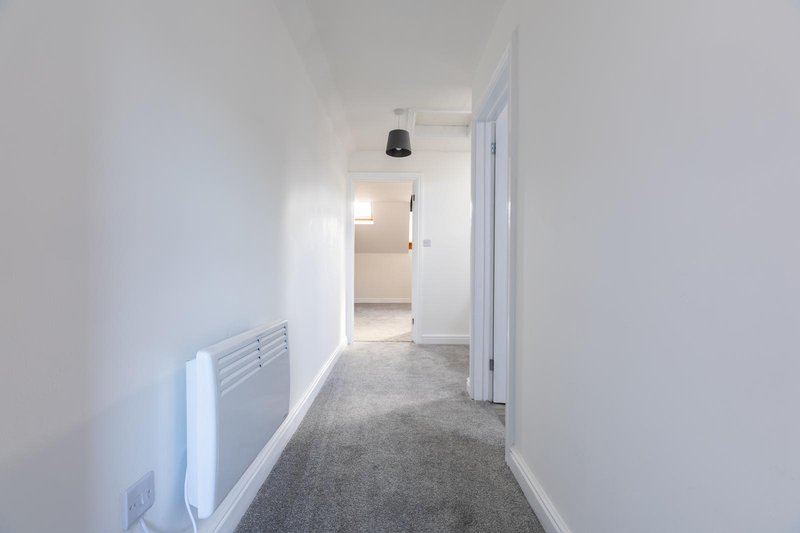 Bright hallway with white walls, grey carpet, radiator and open doors