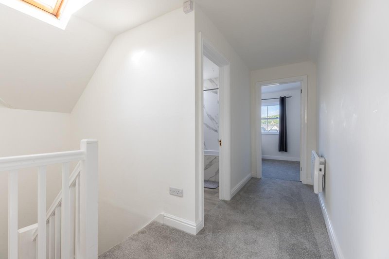 Bright upstairs hallway with gray carpet, white walls, skylight, and open doorways