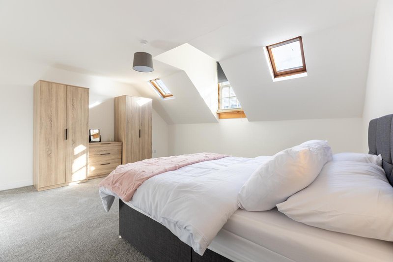 Bright attic bedroom with double bed, wooden wardrobes, skylights and neutral décor