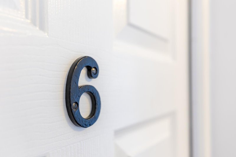 House number 6 mounted on white exterior wall with door visible