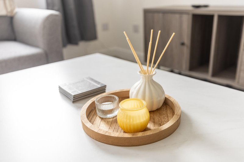 Modern living room with white table, wooden tray with candle and diffuser, grey sofa