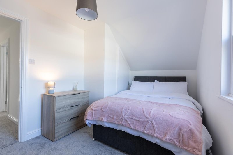Bright attic bedroom with double bed, pink duvet, wooden nightstand and pendant light