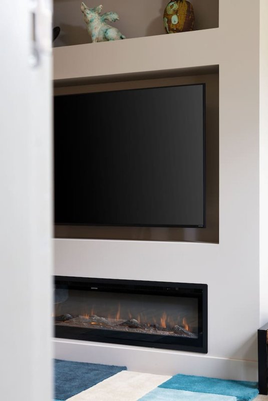 Modern living room with wall-mounted flat-screen TV, electric fireplace insert, and built-in shelving with decorative items