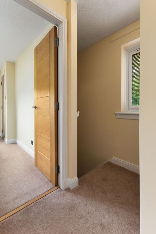 Hallway with wooden door, beige walls, carpet flooring and window