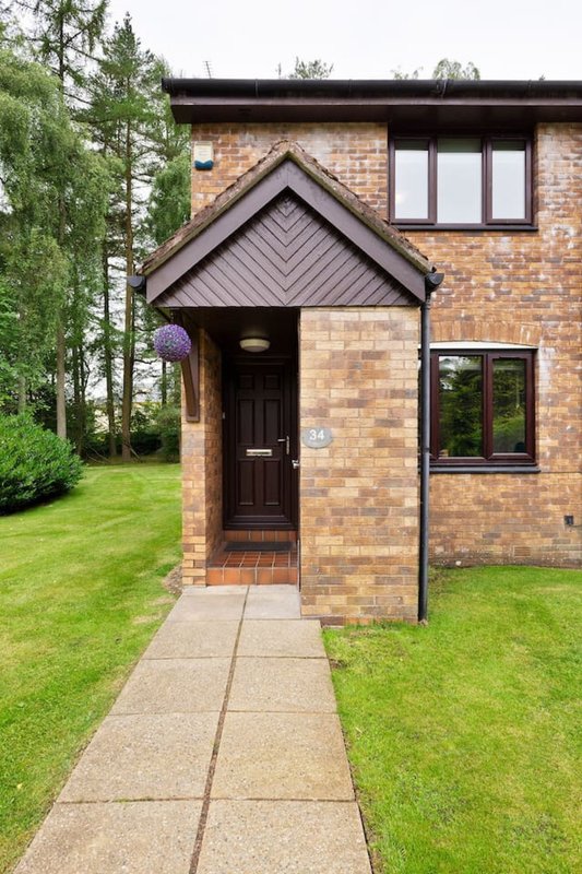 Brick house exterior with dark door, pitched roof entrance, pathway and green lawn