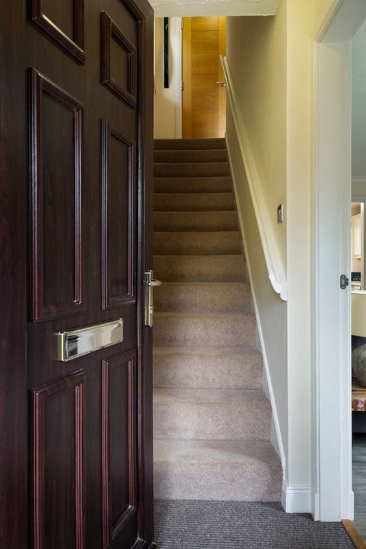 Hallway with dark wooden front door, carpeted stairs leading upward, white walls and handrail