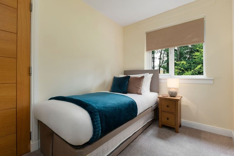 Bright bedroom with single bed, teal bedding, wooden nightstand and window with garden view