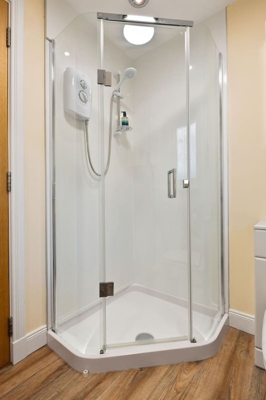 Modern shower enclosure with glass doors, white walls, and wooden floor in bathroom