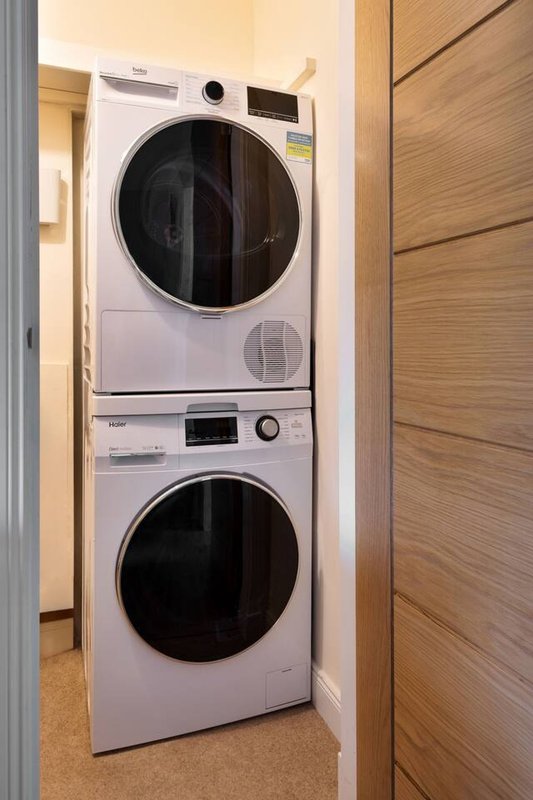 Stacked white washing machine and dryer in utility alcove with wooden door