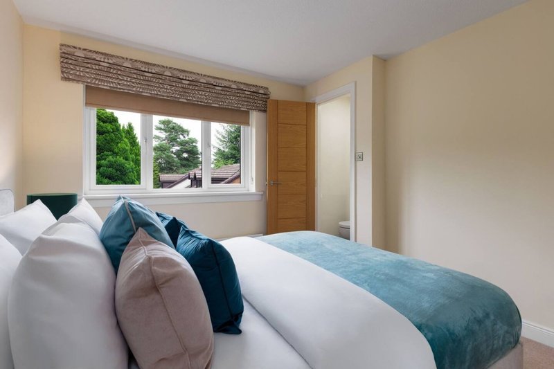 Bright bedroom with double bed, blue bedding, decorative pillows and window with garden view