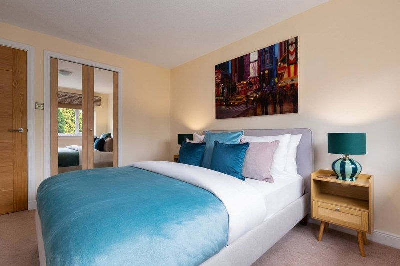 Bright bedroom with double bed, blue bedding, wooden nightstand, and cityscape wall art
