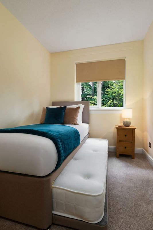 Bright bedroom with single bed, teal bedding, wooden nightstand and window with blind