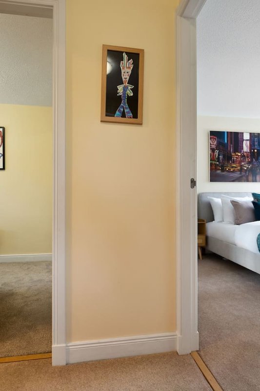 Hallway with yellow walls, framed artwork, and doorways leading to bedroom and bathroom