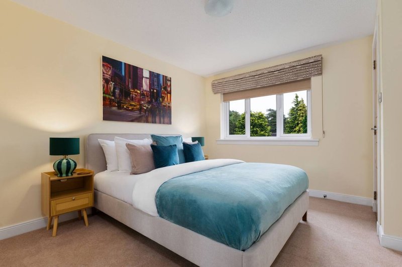 Bedroom with double bed, teal bedding, wooden nightstand, wall art and windows
